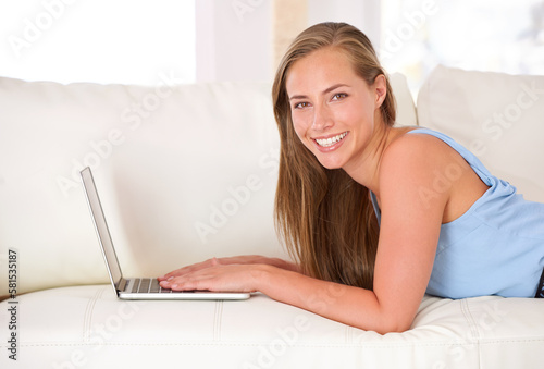 Updating my status. Portrait of an attractive young woman using a laptop while lying on the sofa.