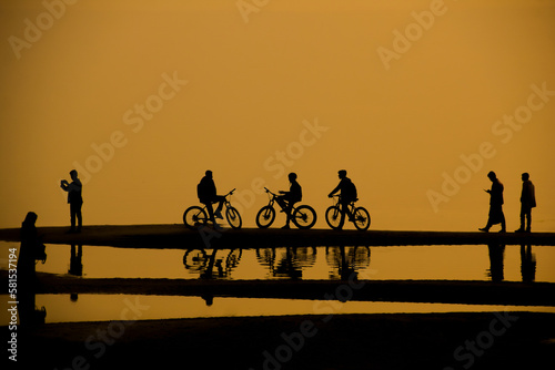 silhouettes of some cyclists on the beach just before sunset