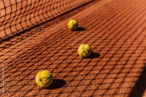 Light orange empty outdoor clay court surface dry grungy ground baseline detail for playing tennis with net shadow in sunny day, yellow green balls, gravel texture background, copy space for text 