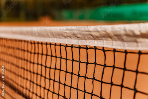 Light orange empty outdoor clay court surface dry grungy ground baseline detail for playing tennis with net in sunny day, gravel texture background, copy space for text inscription banner

