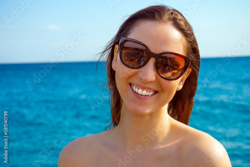 Side view of beautiful mature woman wearing sunglasses at beach. Young smiling woman on vacation looking away while enjoying sea breeze wearing straw hat. Closeup portrait of attractive girl relaxing.