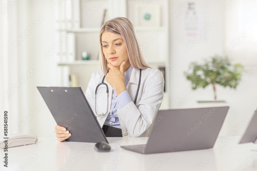 Young female doctor sitting in an office and looking at a document Young female doctor sitting in an office and looking at a document