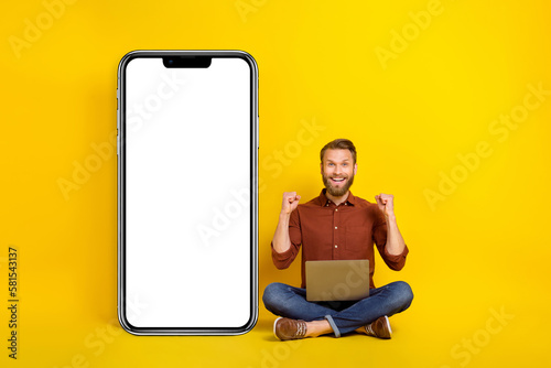 Full size photo of impressed ecstatic man burgundy shirt clench fists laptop win bet sit empty space isolated on yellow color background