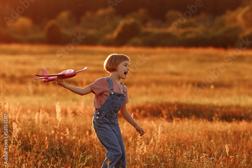 The girl runs across the summer field and launches a toy plane into the sky. A child plays aviator or pilot in a field at sunset, a happy childhood.
