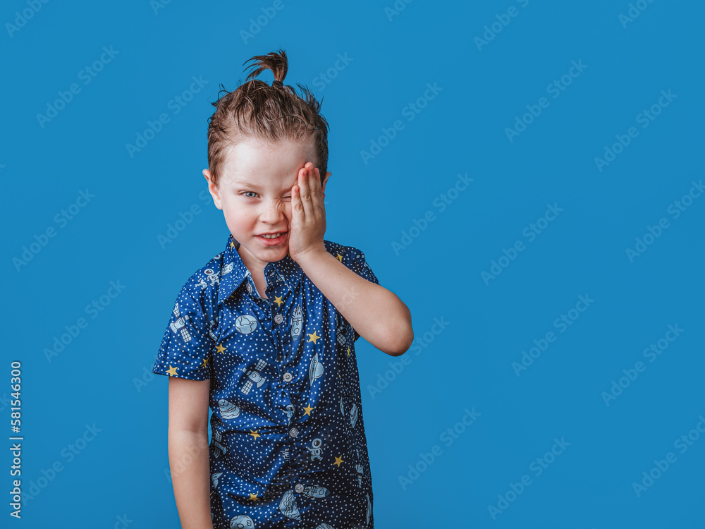 adorable funny boy with ponytail, covers one eye with his hand adorable funny boy with ponytail, covers one eye with his hand