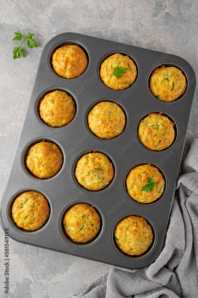 Homemade zucchini muffins with cheese, garlic and herbs in a baking form on a gray concrete background. Vegetarian dish. Copy space, top view. Homemade zucchini muffins with cheese, garlic and herbs in a baking form on a gray concrete background. Vegetarian dish. Copy space, top view.