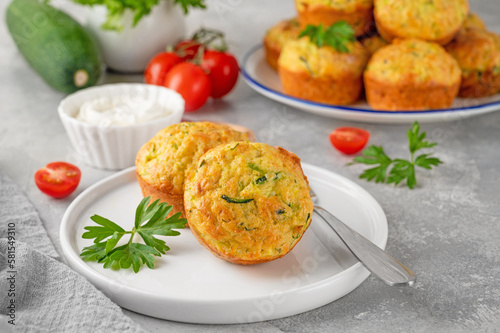 Homemade zucchini muffins with cheese, garlic and herbs on a plate on a gray concrete background. Vegetarian dish. Copy space.
