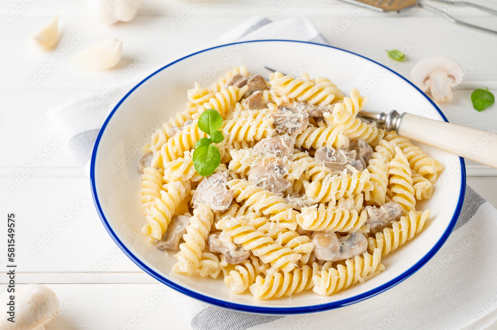 Fusilli pasta with mushrooms, cheese and fresh basil in a plate on a white wooden background.
