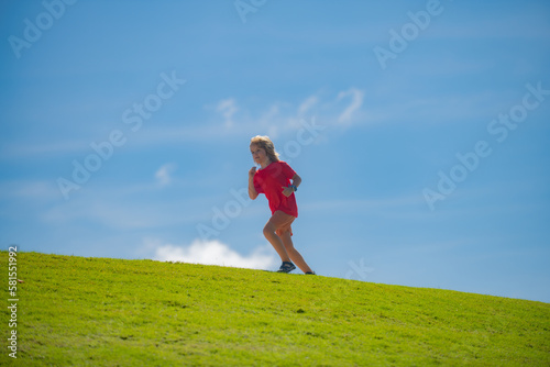 Cute boy running across grass and summer sky. Sporty child boy runner running in summer park. Active kids, sport children.