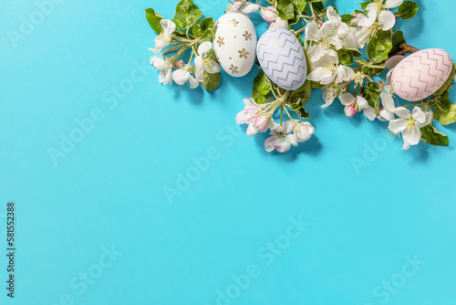 Easter composition with colorful eggs and flowers of apple tree on a blue background. Spring concept, flowers composition. Greeting card. View from above.