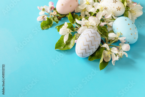 Easter composition with colorful eggs and flowers of apple tree on a blue background.  Spring concept, flowers composition. Greeting card. Copy space.