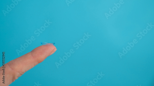 Woman holding contact lens on blue background. Widescreen. 