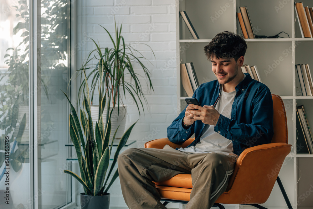 Naklejka premium young man at home looking at mobile phone on the sofa