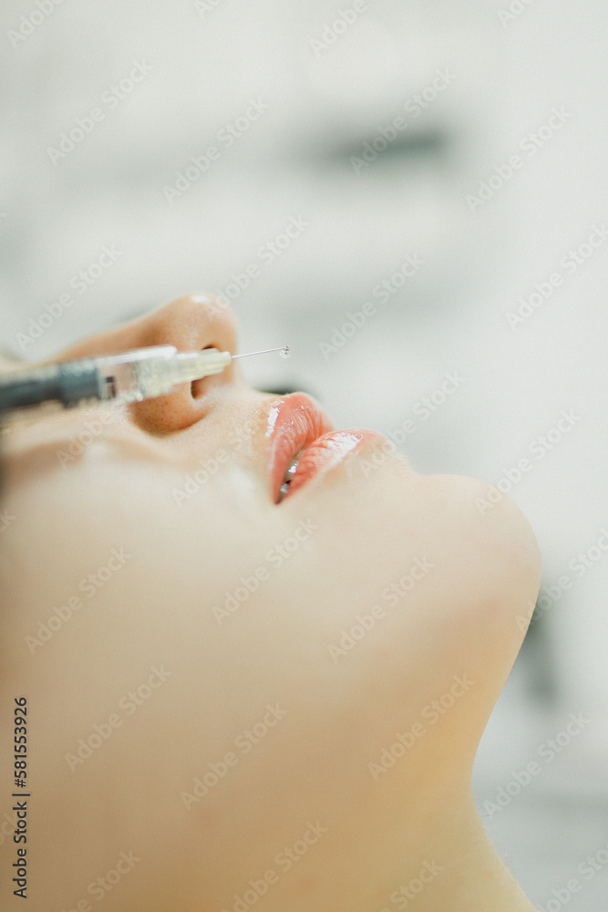 Naklejka premium The cosmetologist makes an injection in the lips of a girl for an increase in the cosmetology office with a syringe close-up face