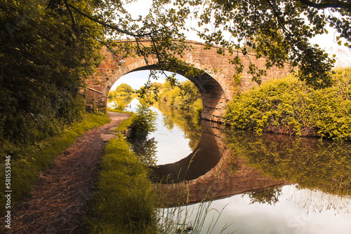 A beautiful scenic and postcard shot of a bridge crossing over the Leeds to Liverpool Canal, the reflection of the bridge clearly visible in the water.