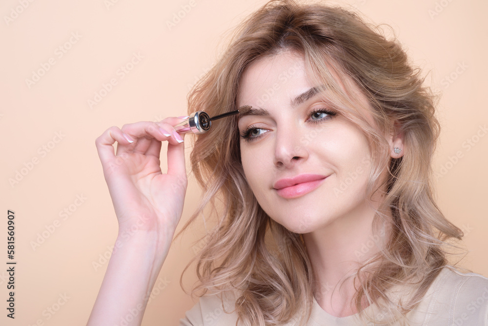 Beautiful woman applies brow gel with brows brush to her eyebrow. Studio portrait of young woman doing her eyebrow natural make up. Eyebrows make up concept.