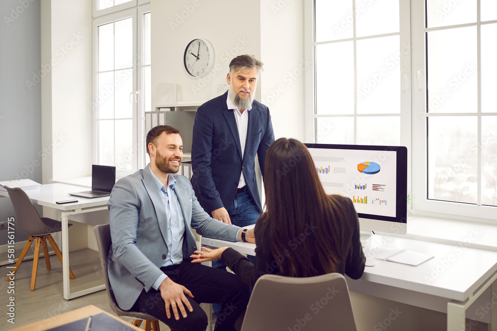 Business team having a work meeting. Group of people talking in the office. Two men and one woman discussing their strategy and using different graphs and charts on the computer screen Business team having a work meeting. Group of people talking in the office. Two men and one woman discussing their strategy and using different graphs and charts on the computer screen