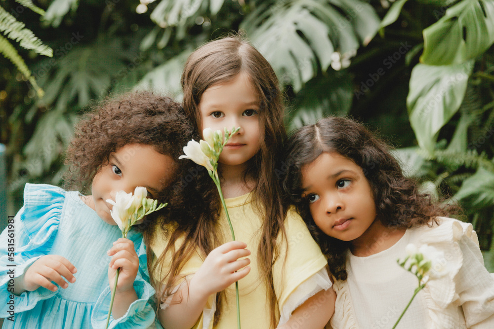 Three little girls in the garden with flowers in their hands. children of different nationalities. Three little girls in the garden with flowers in their hands. children of different nationalities.