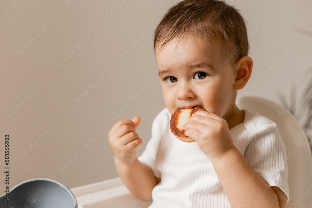 cute baby is sitting in a high chair eating cheesecakes. The concept of baby food. Space for text cute baby is sitting in a high chair eating cheesecakes. The concept of baby food. Space for text