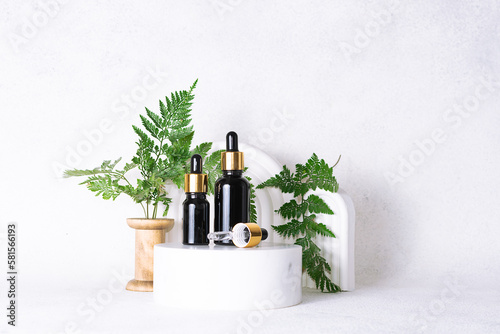 Set of natural organic skin care serums in glass bottles with dropper on white marble background with clay geometric decorations and fern leaves close up. Skin care concept.