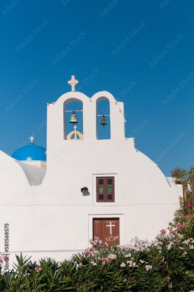 Facade of a white-walled Orthodox church with a bellflower against the blue sky on the island of Santorini in Greece
