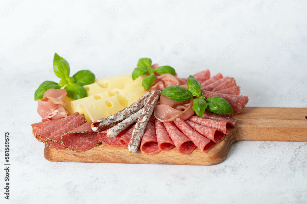 Cheese, prosciutto, salami on a wooden square board.