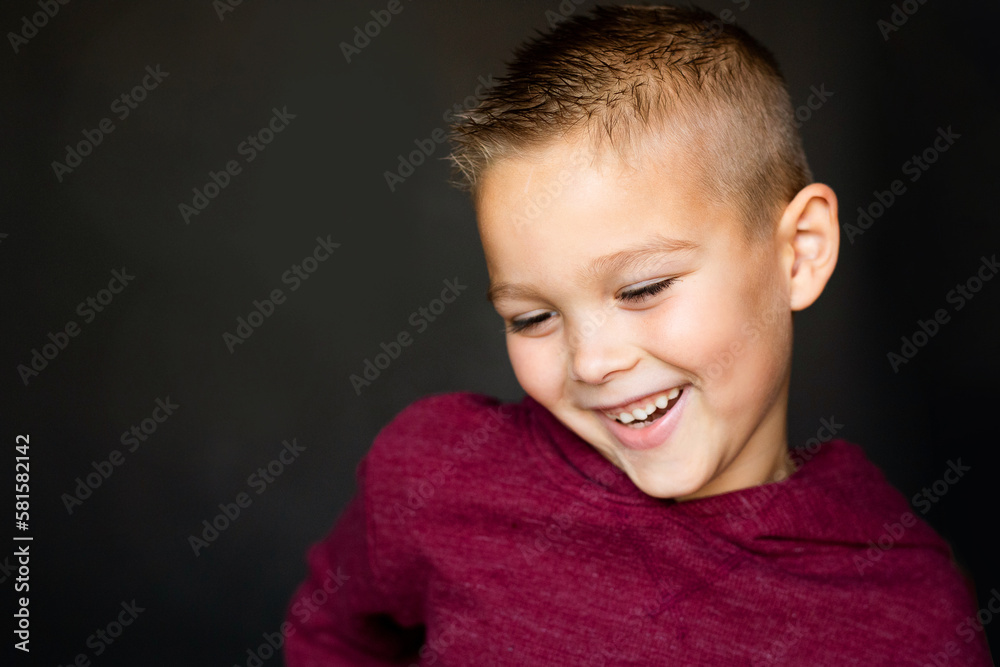 Portrait of a boy smiling, looking down, with a plain black background Portrait of a boy smiling, looking down, with a plain black background