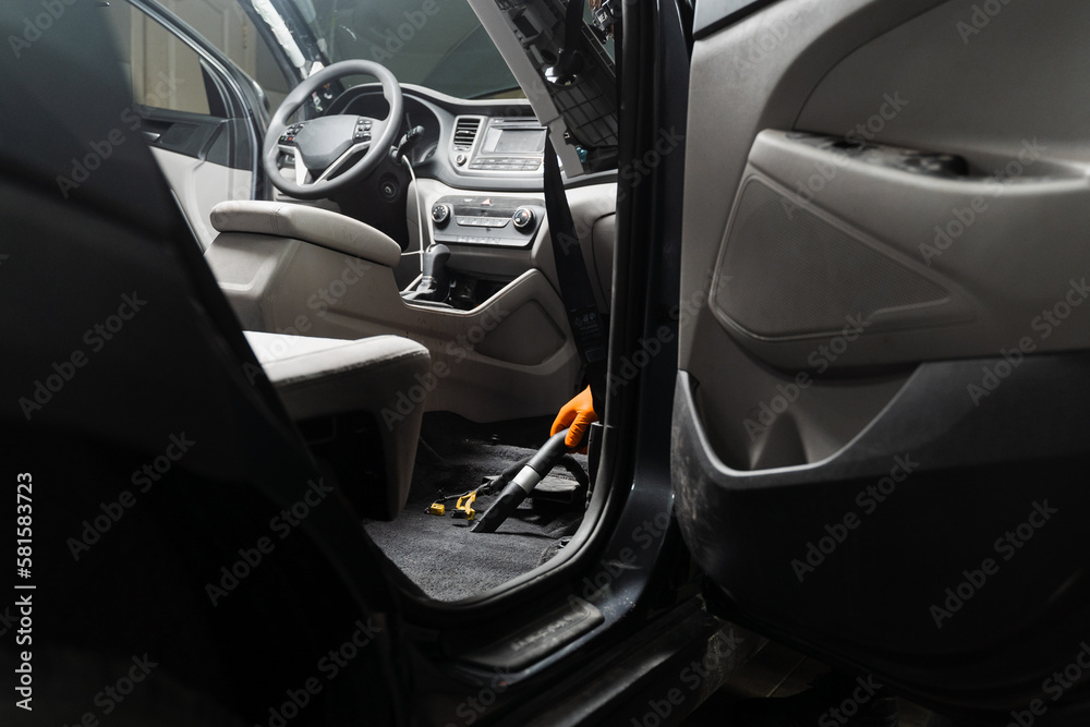 Worker of detailing service is using vacuum cleaner for remove dust and dirt in car. Vacuum cleaning of dirty car floor with removed seats in detailing service.