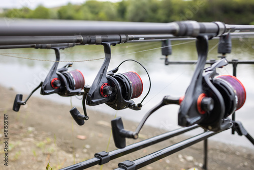 Three rods with reels on stand ready for carp fishing in a beautiful lake. Spools of coiled purple line close up.