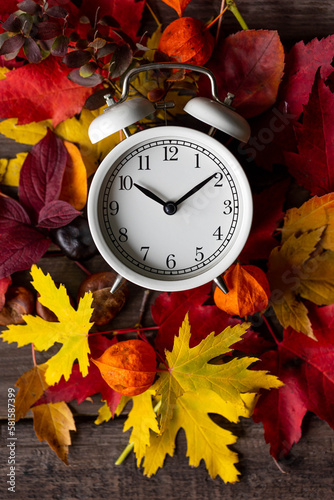 Fall winter time change concept. Autumn composition with retro alarm clock, bright yellow and red leaves, walnut. Brick wall on background. Cozy home atmosphere. Close-up flat lay top view