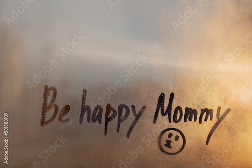 Handwritten text Be happy Mommy with kissing doodle face on orange sunset wet window photo
