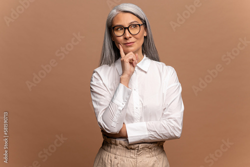 Portrait of thoughtful asian woman in white shirt pondering serious issues, looking with uncertain hesitant expression, making difficult choice. Indoor studio shot isolated on beige background photo
