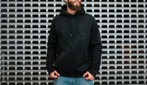 City portrait of handsome hipster man with beard wearing black blank hoodie or hoody and hat with space for your logo or design. Mockup for print