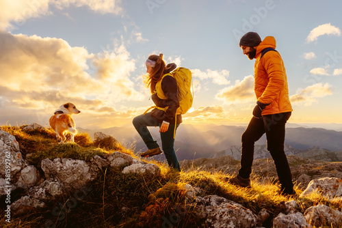 couple of two mountaineers with their adopted dog on a mountain route at sunset. Traveling and playing sports with pets. outdoor activities and adventure. © Alberto