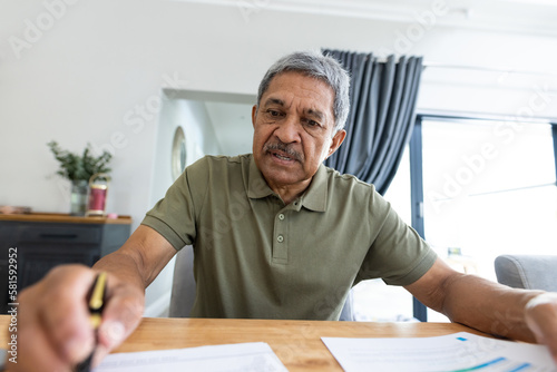 Focused biracial senior man analyzing bills on wooden table while sitting at home