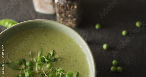 Close up of white bowl of pea soup with peas and seasoning on dark background