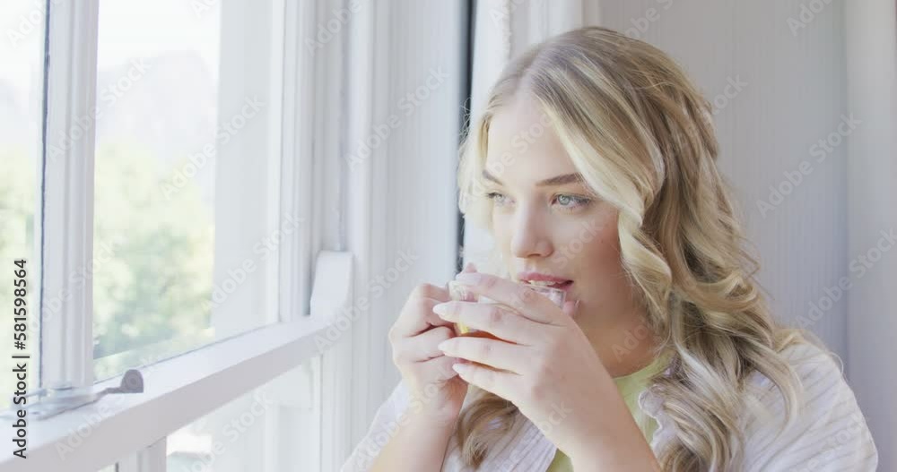 Happy caucasian plus size woman looking through window and drinking tea in slow motion Happy caucasian plus size woman looking through window and drinking tea in slow motion
