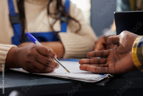 African american delivery service worker searching parcel code in clipboard. Postal warehouse employees checking goods inventory documentation and taking notes hands close up