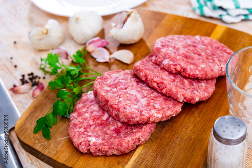 Farmer's uncooked beef and pork burgers for BBQ, grilling or frying on a wooden chopping board in the home kitchen