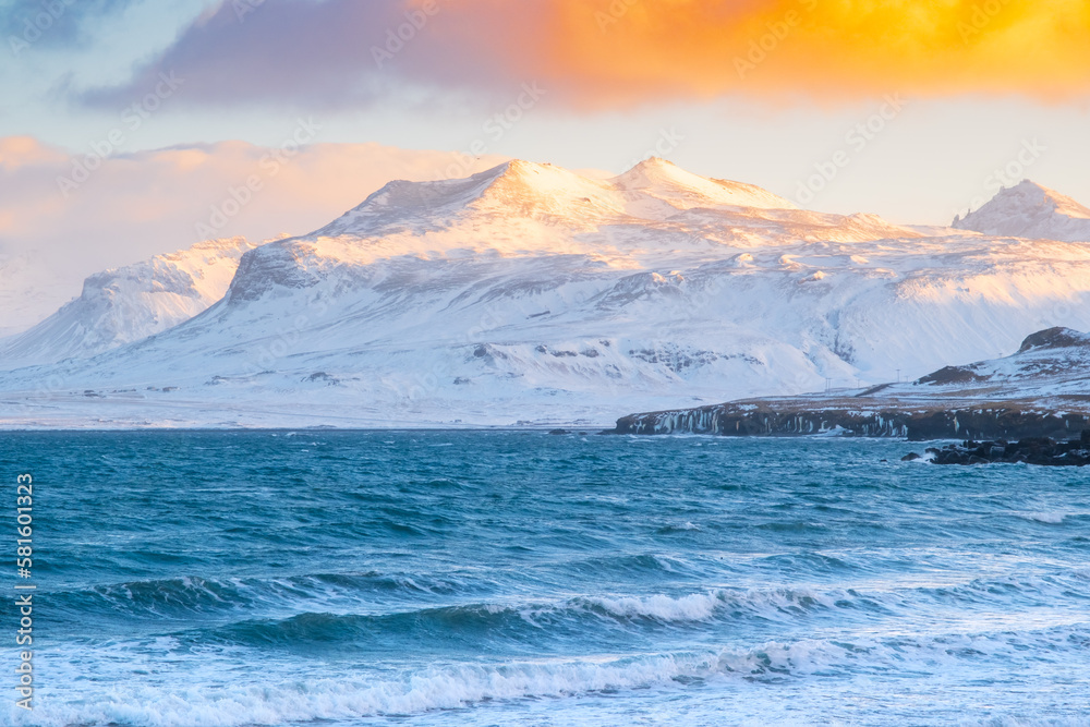 Scenic Winter Atlantic Ocean Coast at Sunset. Snow Covered Mountains in Iceland. Icelandic Fjords During Stormy Weather. Clouds Illuminated by the Warm Rays of the Sun.