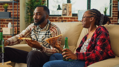 Fotografiet African american people eating slices of pizza in front of tv, binge watching favorite show at home