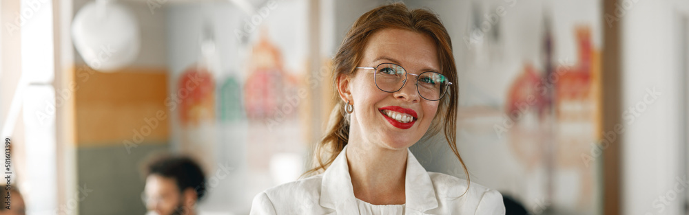 Portrait of smiling businesswoman in white suit standing in modern office on colleagues background Portrait of smiling businesswoman in white suit standing in modern office on colleagues background