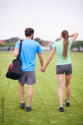 Staying in shape together. A young couple walking hand in hand across a sportsfield.