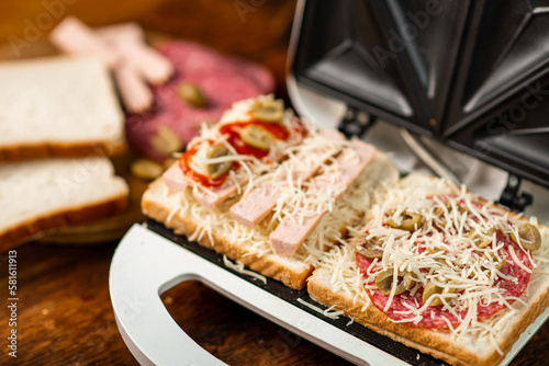 open sandwich maker with cheese toast and sausages. Sandwiching.