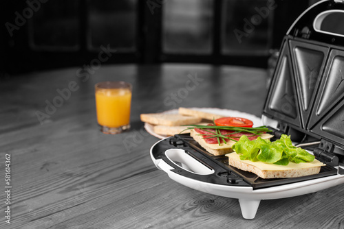 Appetizing sandwiches with ham and herbs in a sandwich maker on a black and white background.