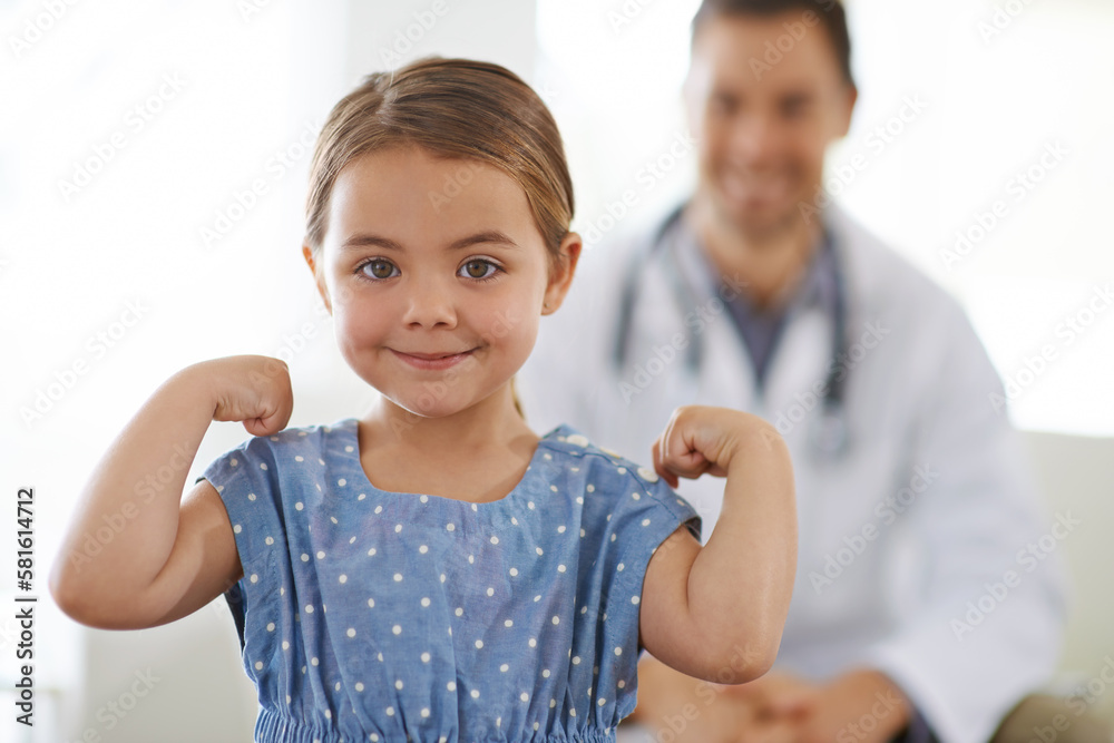 Healthy and strong. A little girl flexing her muscles with her doctor in the background.