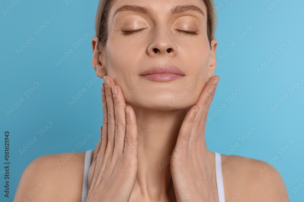 Woman massaging her face on turquoise background Woman massaging her face on turquoise background