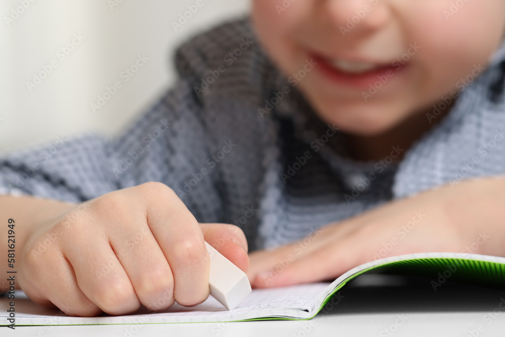Little boy erasing mistake in his notebook at white desk, closeup Little boy erasing mistake in his notebook at white desk, closeup