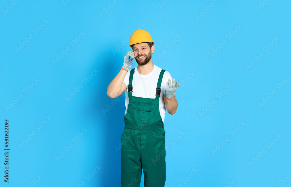 Professional repairman in uniform talking on smartphone against light blue background