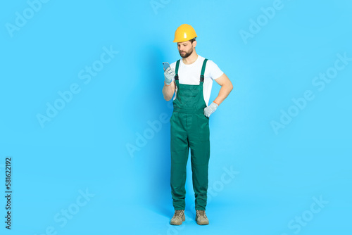 Professional repairman in uniform with smartphone on light blue background